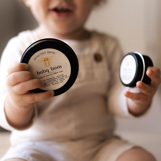 An infant holding jars of all natural tallow based organic moisturizer that is safe for babies developed by honeybee hippie