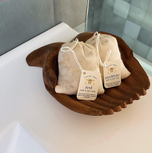 A photo showing two full bags of natural bath salts resting in a wooden bowl in a bathroom